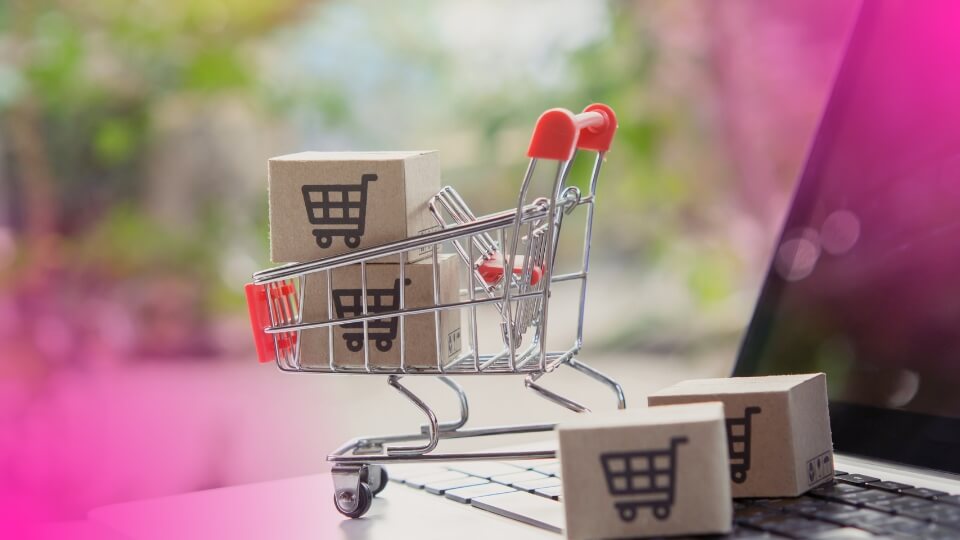 Carrinho de compras com caixas sobre notebook, representando disputa pela Buy Box em marketplaces.