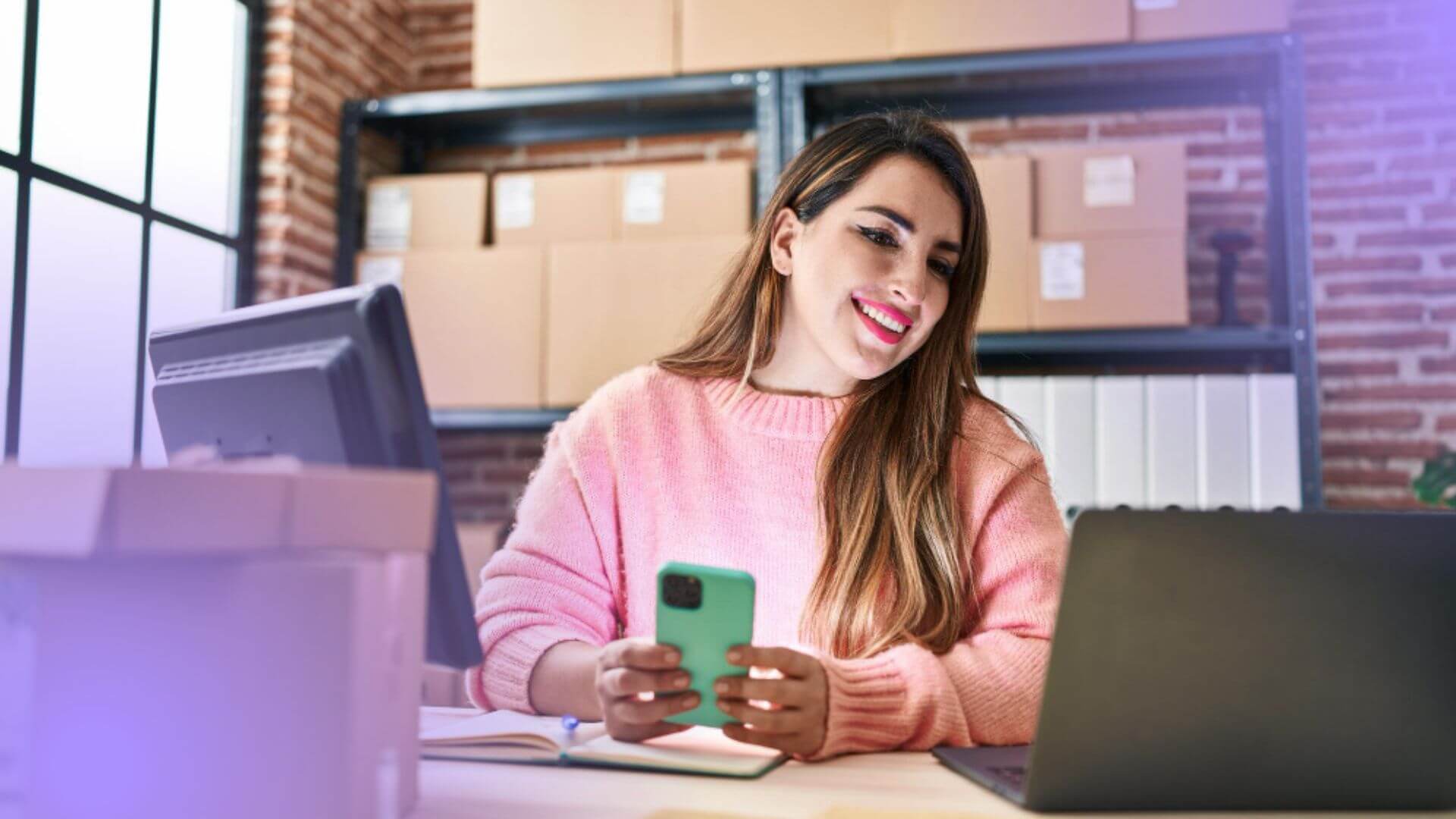 Empreendedora usando celular e notebook em estoque de produtos, representando a rotina de quem deseja vender na Shopee.