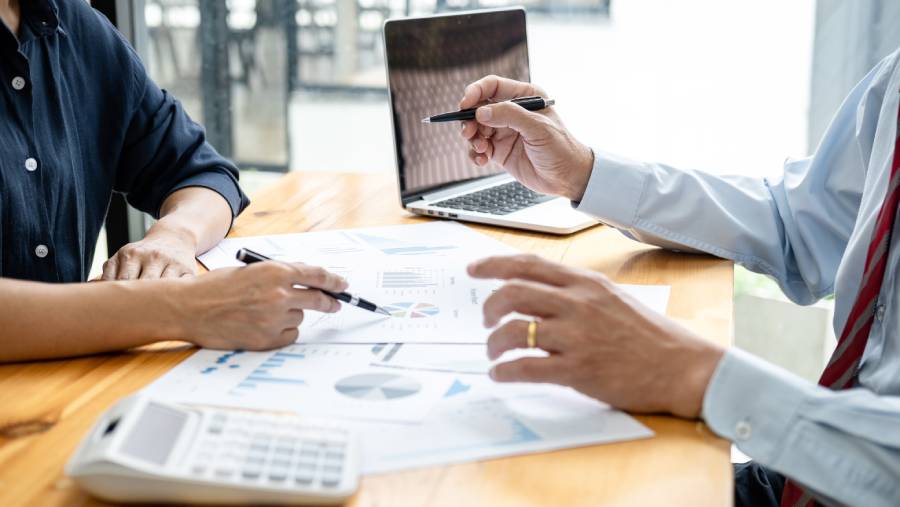 Dois profissionais revisando gráficos e relatórios sobre a mesa com laptop e calculadora, discutindo estratégia de vendas online com base em métricas