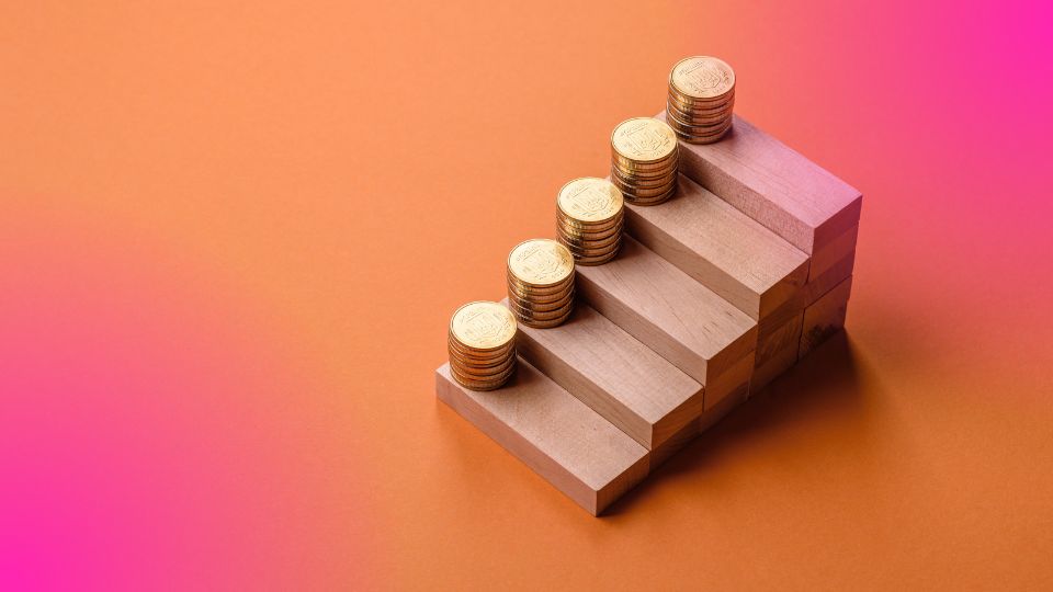 Pilhas de moedas douradas crescendo em degraus de madeira, ilustrando a diferen&ccedil;a entre markup e margem no crescimento financeiro