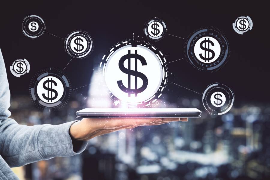 Mão segurando tablet com ícones de cifrão flutuantes representando gestão digital de markup e margem em marketplaces