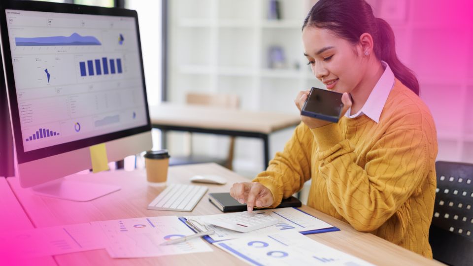 Mulher de su&eacute;ter amarelo analisando relat&oacute;rios financeiros e usando calculadora enquanto gerencia an&uacute;ncios no Mercado Livre ao telefone