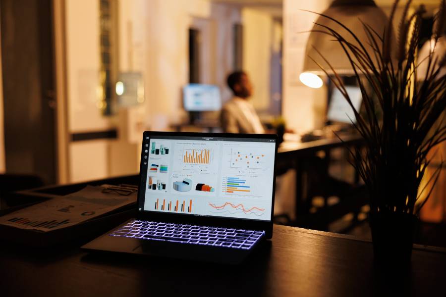 Laptop com dashboard de gráficos e métricas aberto sobre mesa em escritório escuro, representando a gestão de anúncios no Mercado Livre