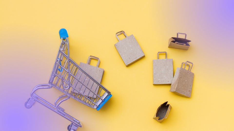 Carrinho de compras miniatura tombado com sacolas ao redor, representando volume de pedidos em campanha ads no Mercado Livre